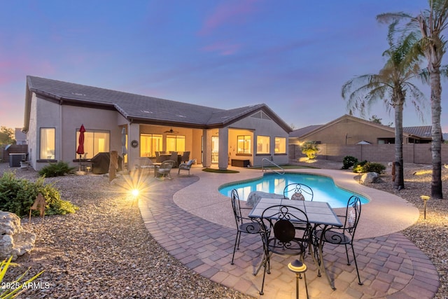 pool at dusk featuring outdoor dining area, a fenced backyard, a fenced in pool, a ceiling fan, and a patio area