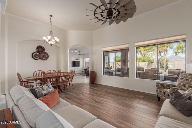 living area with crown molding, arched walkways, a notable chandelier, and wood finished floors