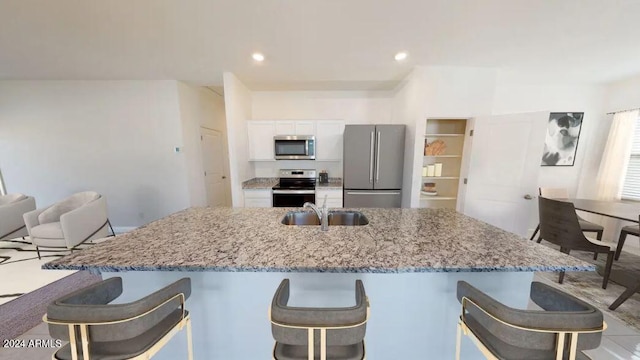 kitchen with white cabinetry, sink, light stone countertops, stainless steel appliances, and a kitchen breakfast bar