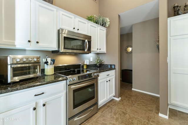 kitchen with light tile patterned floors, stainless steel appliances, dark stone counters, and white cabinets