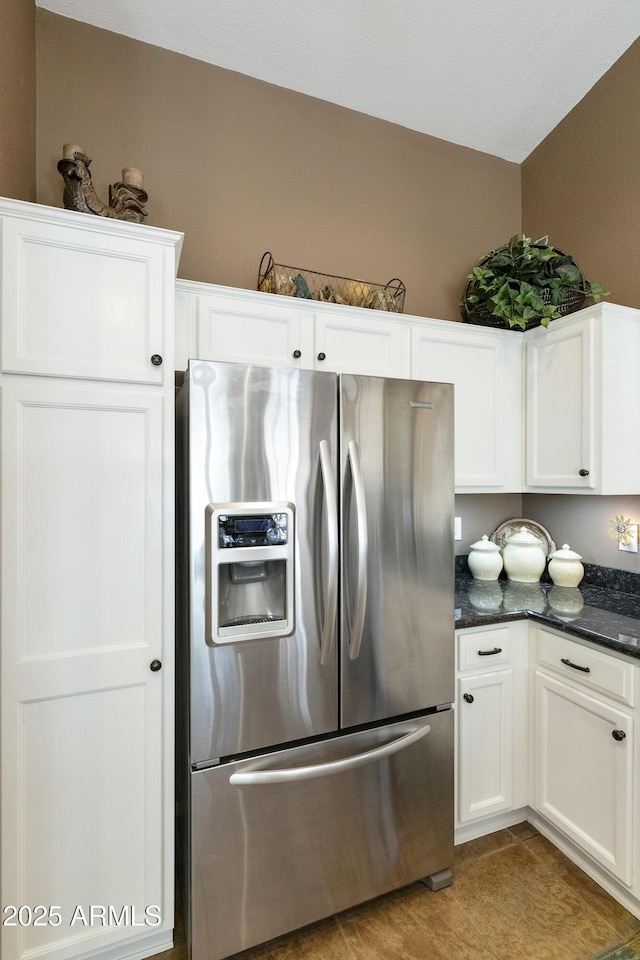 kitchen featuring stainless steel refrigerator with ice dispenser, dark stone countertops, and white cabinets