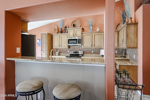 kitchen featuring stainless steel appliances, tasteful backsplash, light stone counters, lofted ceiling, and a breakfast bar area