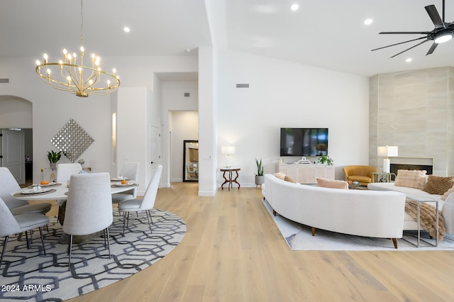 living room with ceiling fan with notable chandelier, light wood-type flooring, high vaulted ceiling, and a tile fireplace