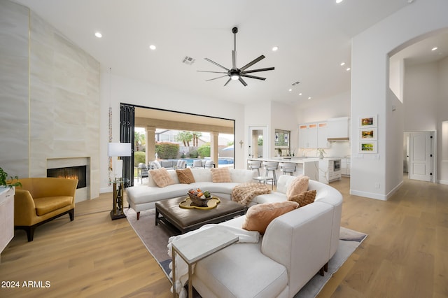 living room with ceiling fan, light wood-type flooring, a high ceiling, and a tiled fireplace