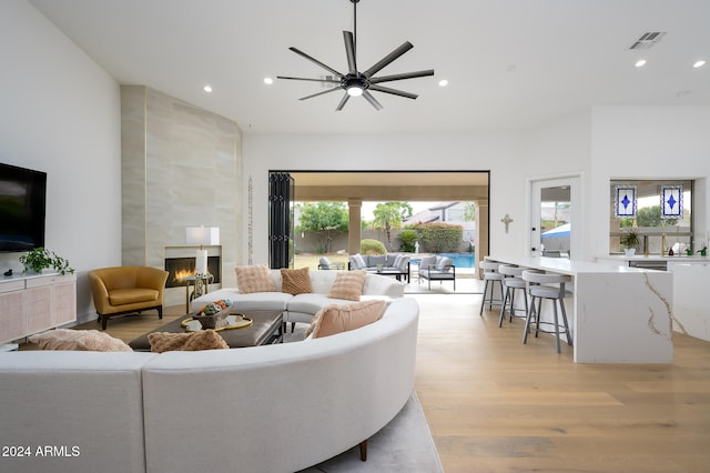 living room featuring light wood-type flooring, ceiling fan, and a tiled fireplace