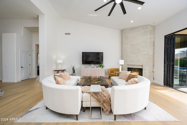 living room featuring a tile fireplace, light wood-type flooring, vaulted ceiling, and ceiling fan