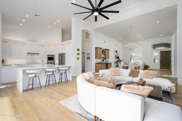 living room with sink, high vaulted ceiling, ceiling fan with notable chandelier, and light wood-type flooring