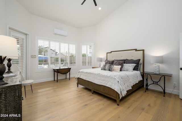 bedroom with high vaulted ceiling, a wall unit AC, and light hardwood / wood-style flooring