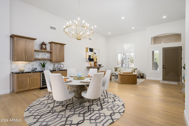 dining space with beverage cooler, light wood-type flooring, a towering ceiling, and an inviting chandelier