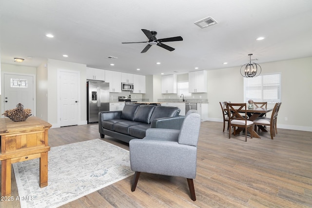 living room with ceiling fan with notable chandelier, light wood-type flooring, and sink