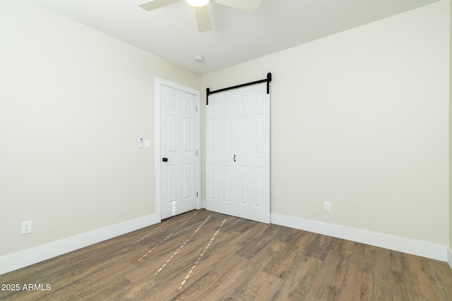 unfurnished bedroom featuring a barn door, ceiling fan, and dark wood-type flooring