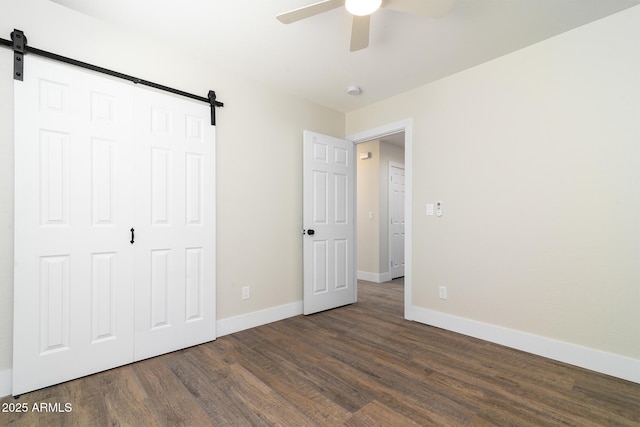 unfurnished bedroom featuring dark hardwood / wood-style flooring, a barn door, a closet, and ceiling fan