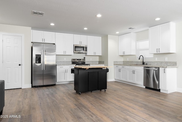 kitchen featuring white cabinetry, sink, stainless steel appliances, light stone counters, and a kitchen island