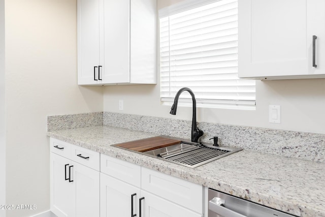 kitchen featuring dishwasher, light stone counters, white cabinetry, and sink