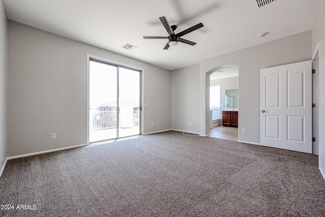 unfurnished room with arched walkways, ceiling fan, carpet floors, visible vents, and baseboards