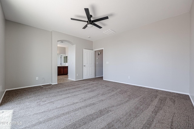 unfurnished bedroom featuring arched walkways, ensuite bathroom, carpet floors, visible vents, and baseboards