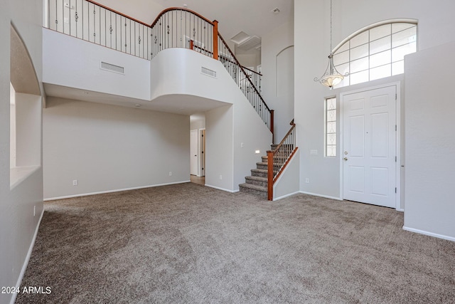 carpeted entrance foyer with stairway, baseboards, a high ceiling, and visible vents