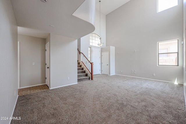 unfurnished living room featuring baseboards, stairs, a high ceiling, and carpet flooring