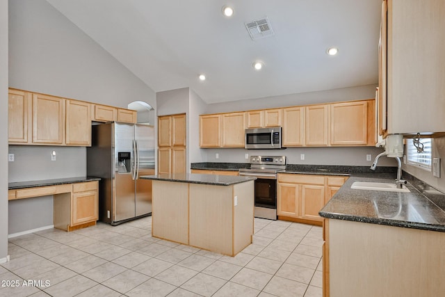 kitchen with stainless steel appliances, light brown cabinetry, a sink, dark stone counters, and light tile patterned flooring