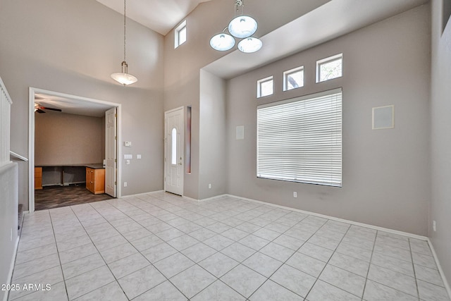 unfurnished room featuring a towering ceiling, light tile patterned floors, baseboards, and a ceiling fan