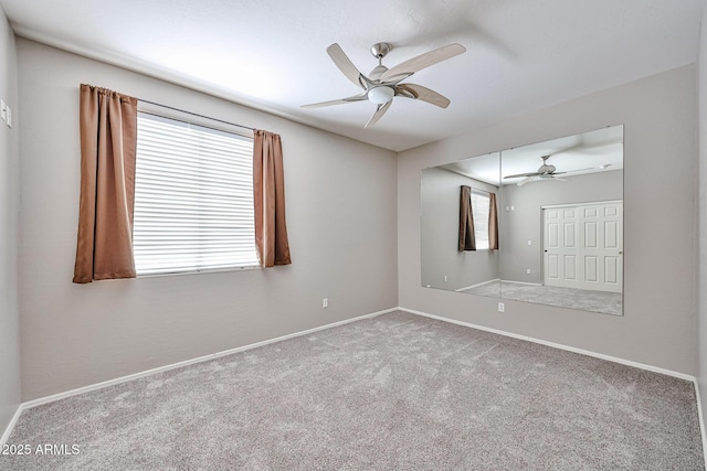 carpeted empty room featuring ceiling fan and baseboards