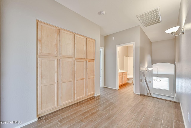 unfurnished bedroom featuring arched walkways, light wood finished floors, baseboards, and connected bathroom