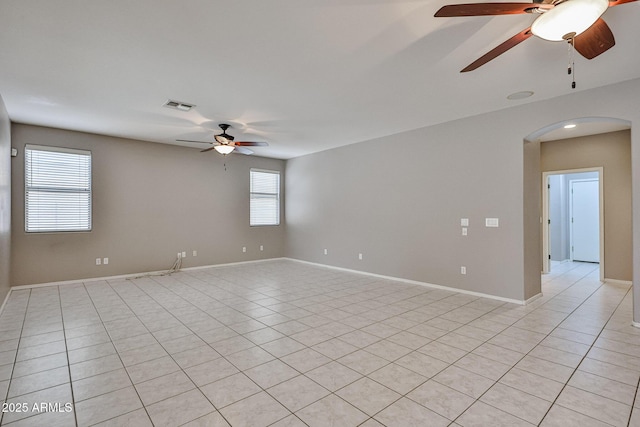 empty room with a ceiling fan, arched walkways, light tile patterned floors, and baseboards