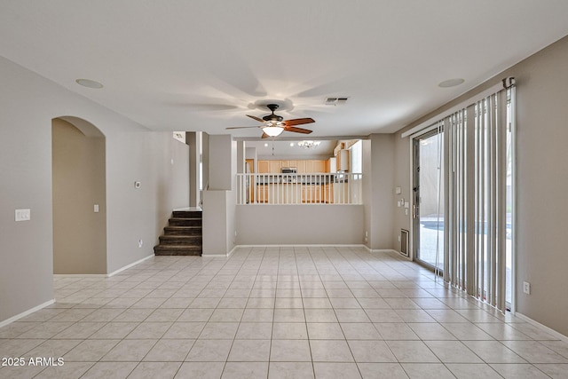 empty room featuring ceiling fan, arched walkways, light tile patterned floors, and stairway
