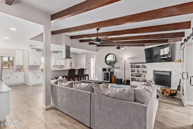 living room featuring beam ceiling, ceiling fan, a barn door, light hardwood / wood-style flooring, and a fireplace