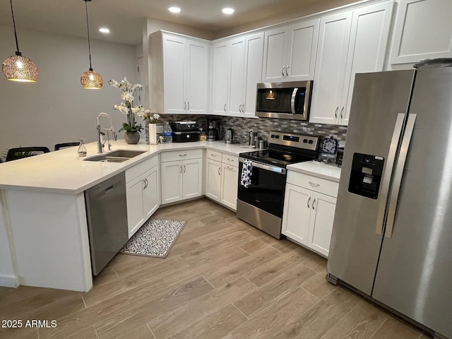 kitchen featuring appliances with stainless steel finishes, kitchen peninsula, pendant lighting, white cabinets, and sink