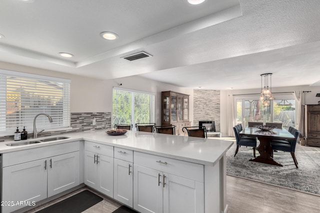 kitchen with sink, white cabinets, hanging light fixtures, kitchen peninsula, and plenty of natural light