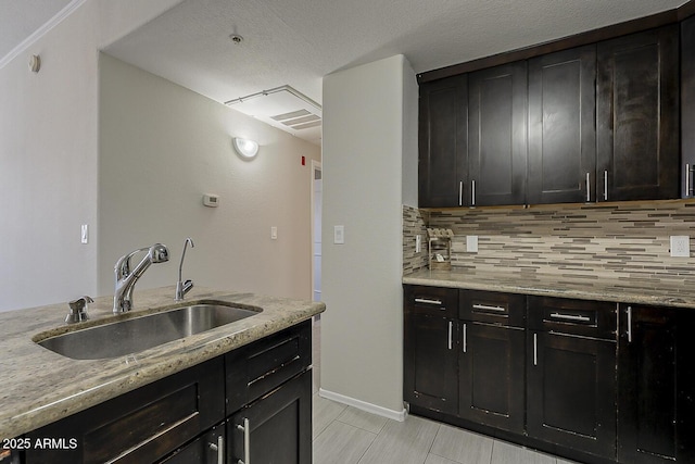 kitchen featuring a sink, light stone counters, decorative backsplash, and baseboards