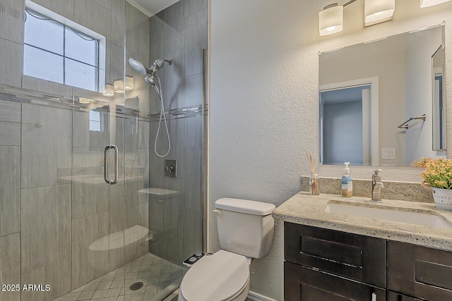 full bath featuring vanity, a textured wall, toilet, and a shower stall