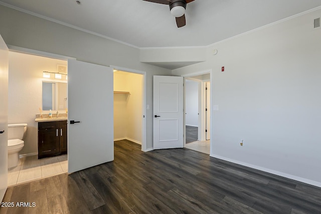 unfurnished bedroom with crown molding, connected bathroom, a sink, dark wood-type flooring, and a spacious closet