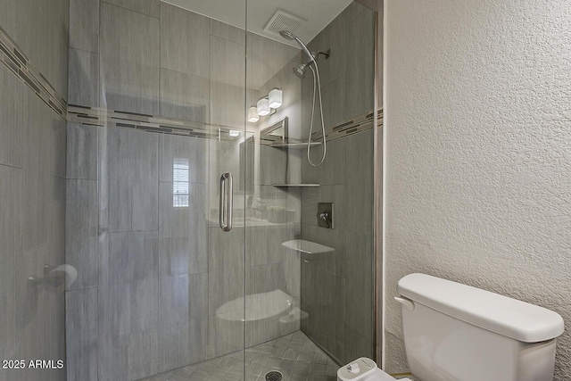 bathroom featuring visible vents, a textured wall, toilet, and a shower stall
