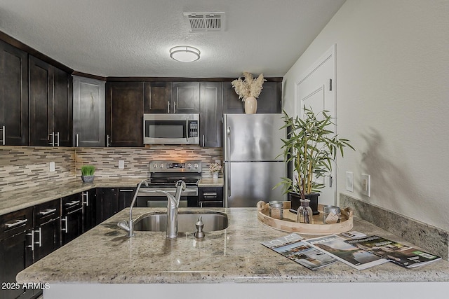 kitchen with visible vents, tasteful backsplash, light stone counters, a sink, and stainless steel appliances