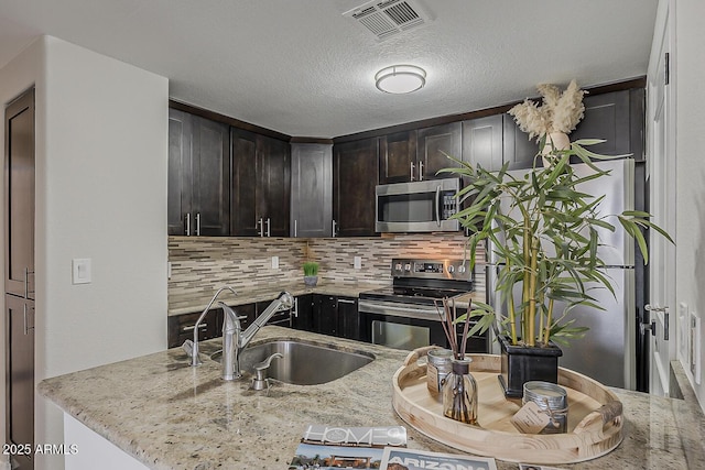 kitchen with decorative backsplash, visible vents, appliances with stainless steel finishes, a sink, and light stone counters