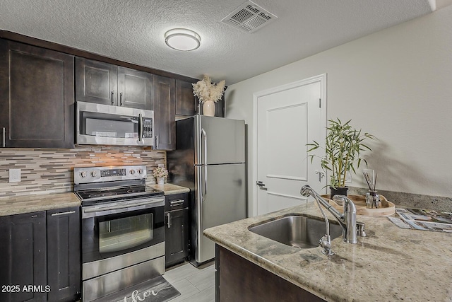 kitchen with backsplash, visible vents, light stone countertops, a sink, and stainless steel appliances