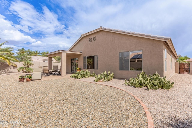 rear view of property with a tile roof, stucco siding, fence, and a patio area