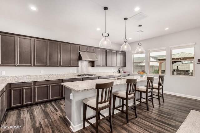 kitchen with visible vents, dark wood finished floors, stainless steel gas stovetop, dark brown cabinets, and under cabinet range hood