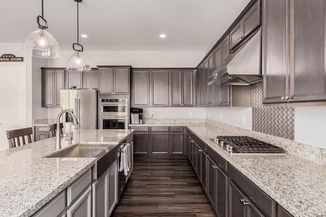 kitchen with pendant lighting, under cabinet range hood, light stone counters, appliances with stainless steel finishes, and dark brown cabinets