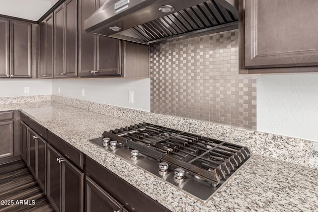 kitchen with range hood, light stone counters, decorative backsplash, dark brown cabinetry, and stainless steel gas stovetop