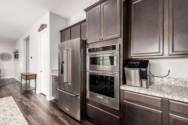 kitchen featuring dark brown cabinets, dark wood-type flooring, baseboards, light stone counters, and appliances with stainless steel finishes