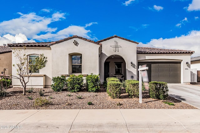 mediterranean / spanish-style home with a tile roof, an attached garage, driveway, and stucco siding