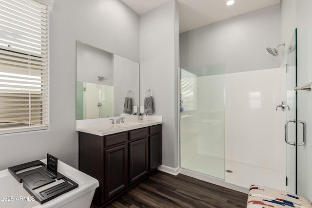 full bath featuring a shower with door, a sink, double vanity, and wood finished floors