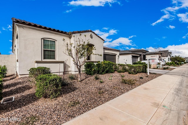 view of side of home featuring a garage, a tile roof, driveway, and stucco siding