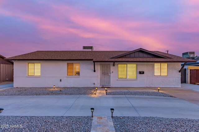 view of front of property featuring concrete driveway, roof with shingles, stucco siding, fence, and central AC unit