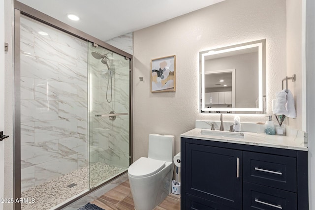 bathroom featuring a marble finish shower, toilet, wood finished floors, vanity, and a textured wall