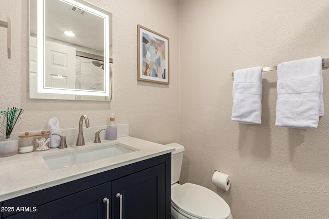 full bath featuring visible vents, a shower, toilet, vanity, and a textured wall