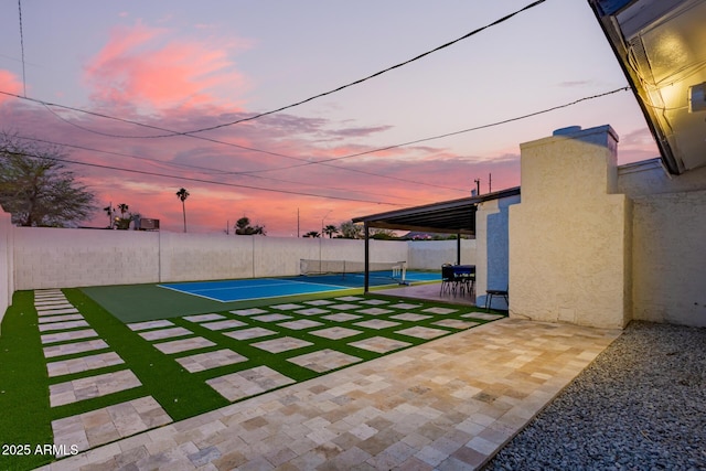 yard at dusk featuring a tennis court and fence